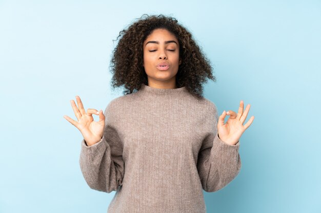 Joven mujer afroamericana aislada en azul en pose zen