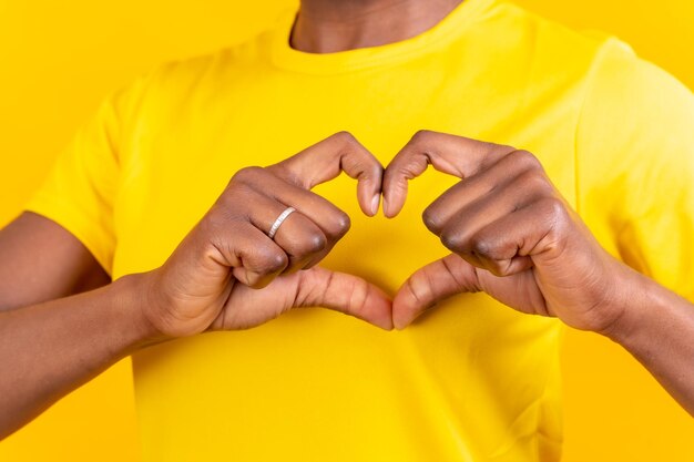 Joven mujer afroamericana aislada en un fondo amarillo sonriendo y sesión de estudio de gesto de corazón