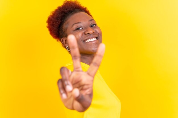 Joven mujer afroamericana aislada en un fondo amarillo sonriendo con la sesión de estudio de gesto de victoria