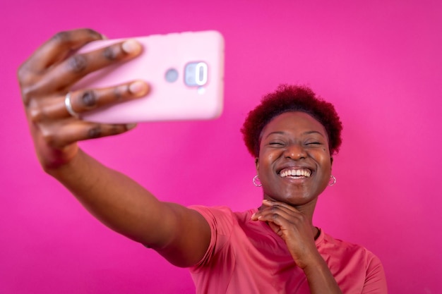 Joven mujer afroamericana aislada en un fondo rosa sonriendo y haciendo una sesión de estudio selfie