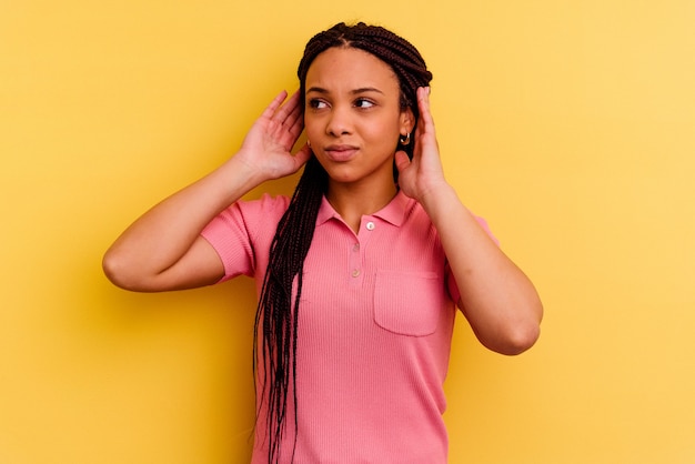 Joven mujer afroamericana aislada en la pared amarilla que cubre las orejas con los dedos, estresada y desesperada por un ambiente ruidoso.
