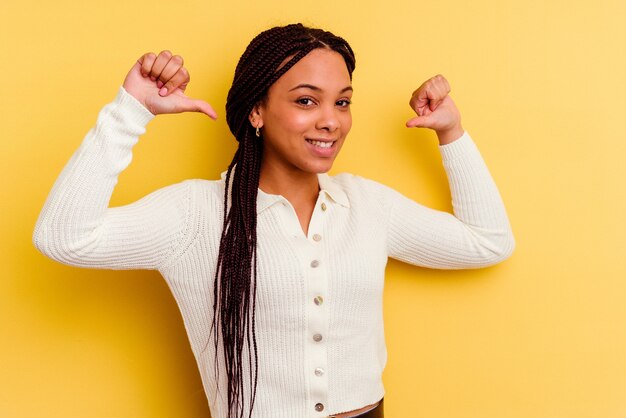 Joven mujer afroamericana aislada en la pared amarilla se siente orgullosa y segura de sí misma, ejemplo a seguir