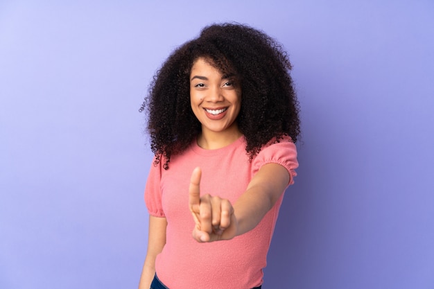 Joven mujer afroamericana aislada en pared púrpura mostrando y levantando un dedo