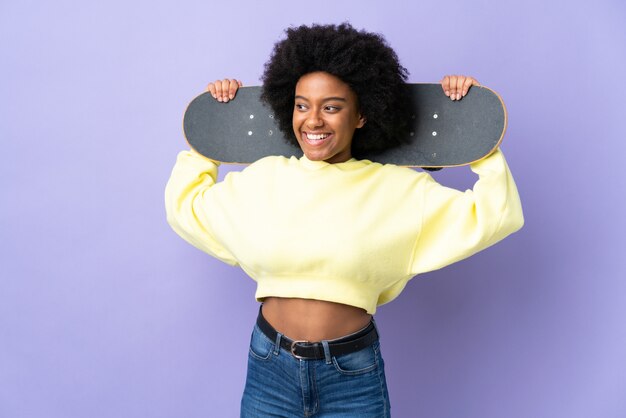 Joven mujer afroamericana aislada en la pared púrpura con un patín con expresión feliz