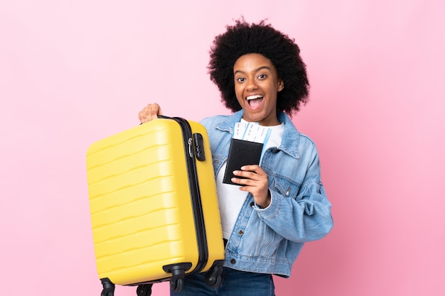 Joven mujer afroamericana aislada en pared rosa en vacaciones con maleta y pasaporte