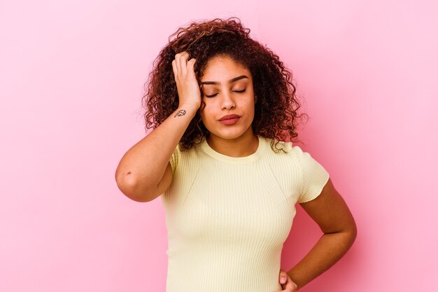 Joven mujer afroamericana aislada en rosa cansada y con mucho sueño manteniendo la mano en la cabeza.