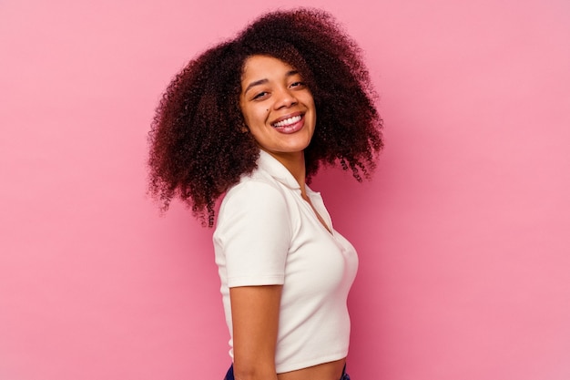 Joven mujer afroamericana aislada en rosa seguro manteniendo las manos en las caderas.