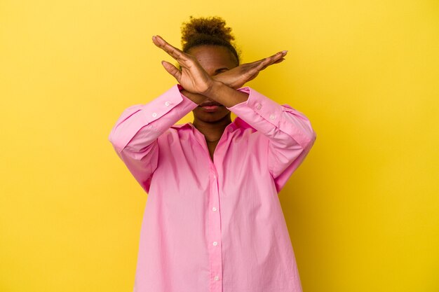 Joven mujer afroamericana aislada sobre fondo amarillo manteniendo dos brazos cruzados, concepto de negación.