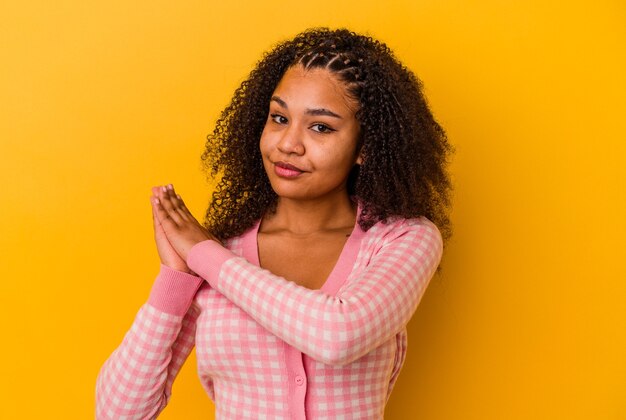 Joven mujer afroamericana aislada sobre fondo amarillo sintiéndose enérgica y cómoda, frotándose las manos con confianza.