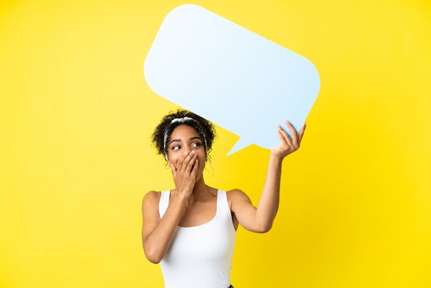 Joven mujer afroamericana aislada sobre fondo amarillo sosteniendo un bocadillo vacío con expresión de sorpresa