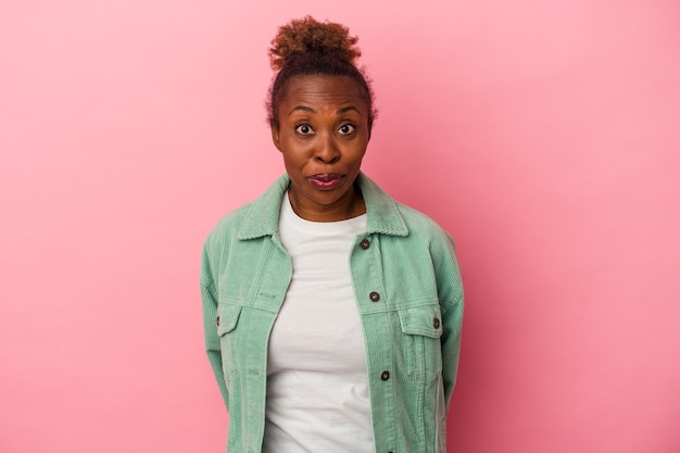 Joven mujer afroamericana aislada sobre fondo rosa se encoge de hombros y abre los ojos confundidos.