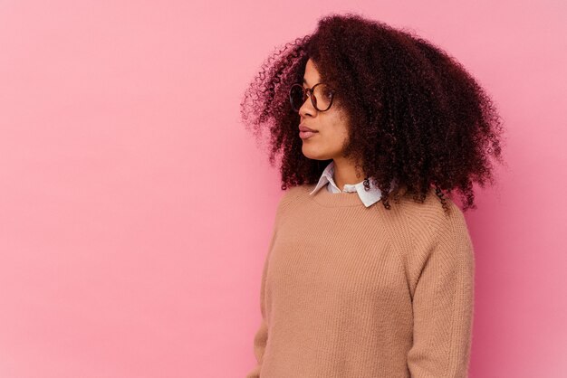 Joven mujer afroamericana aislada sobre fondo rosa mirando a la izquierda, pose de lado.