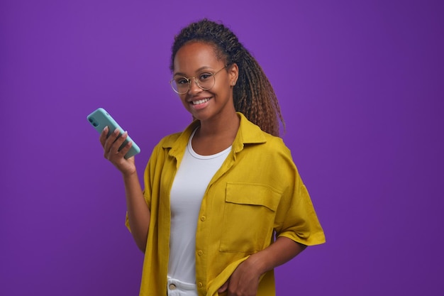 Joven mujer afroamericana alegre con soportes de teléfono sobre fondo lila