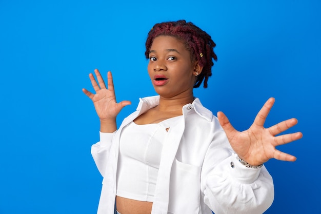 Joven mujer afroamericana asustada y aterrorizada de pie contra el fondo azul.