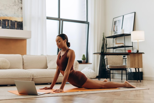 Joven mujer afroamericana atractiva entrenando haciendo ejercicios usando una computadora portátil viendo video