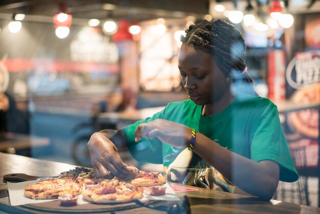 Joven mujer afroamericana auténtica comiendo pizza en el restaurante de la ciudad nocturna