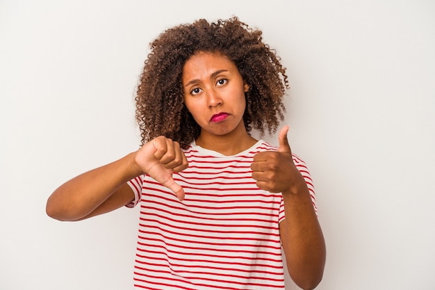 Joven mujer afroamericana con cabello rizado aislado sobre fondo blanco mostrando los pulgares hacia arriba y hacia abajo, concepto difícil de elegir