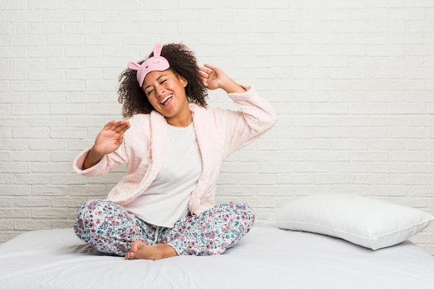 Joven mujer afroamericana en la cama vistiendo pijama bailando y divirtiéndose.