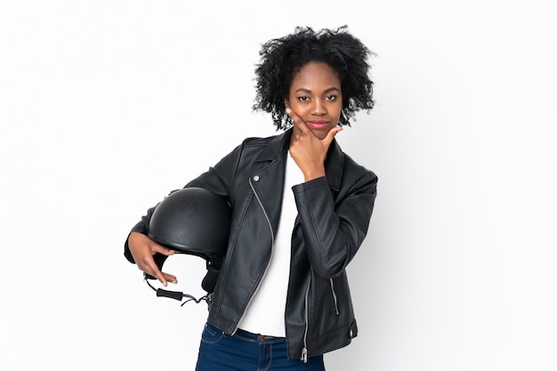 Joven mujer afroamericana con un casco de moto en pared blanca pensando una idea