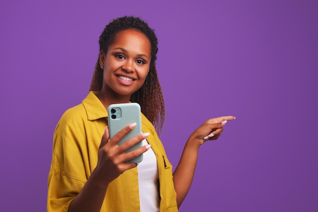 Joven mujer afroamericana casual sonriente con el teléfono señala dedo a lado