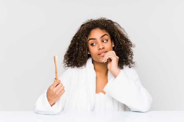 Joven mujer afroamericana con un cepillo de dientes relajado pensando en algo