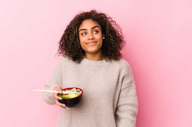 Joven mujer afroamericana comiendo fideos soñando con lograr objetivos y propósitos