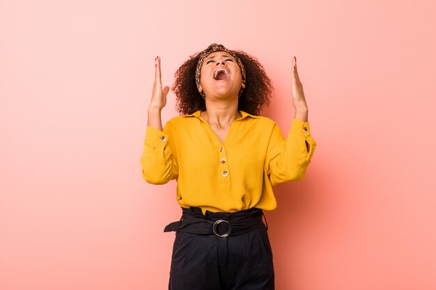 Joven mujer afroamericana contra un fondo rosa gritando al cielo