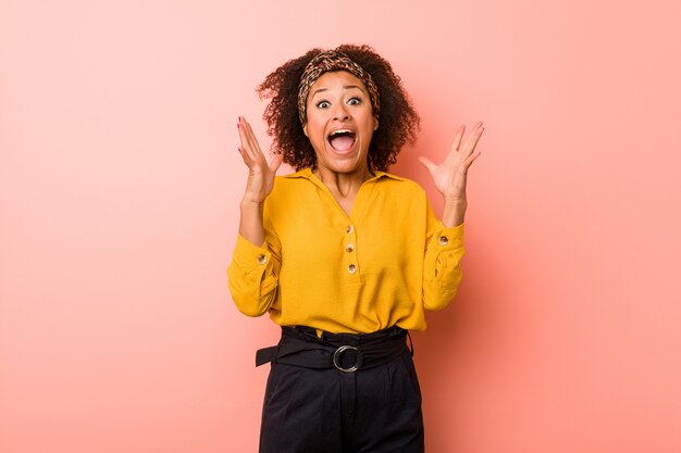 Joven mujer afroamericana contra una pared rosa celebrando una victoria