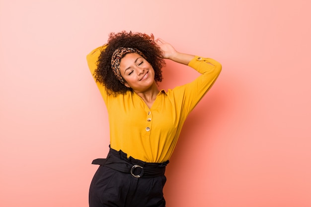 Joven mujer afroamericana contra un rosa estirando los brazos, posición relajada.