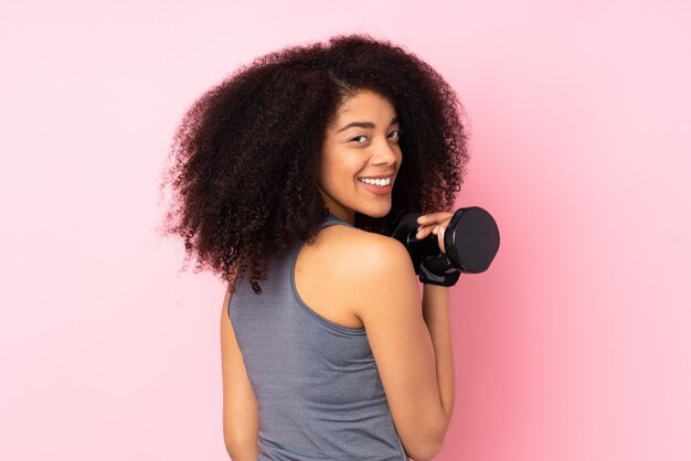 Joven mujer afroamericana deporte en pared rosa haciendo pesas