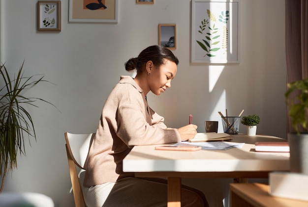 Joven mujer afroamericana escribiendo en un cuaderno en casa con los rayos del sol