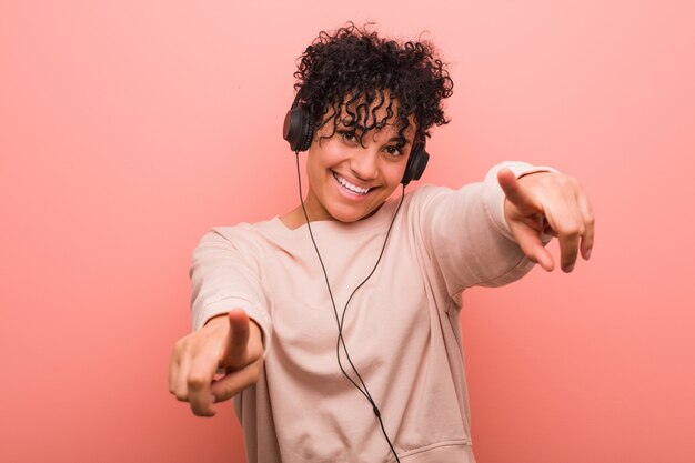 Joven mujer afroamericana escuchando música alegre sonrisas apuntando al frente.