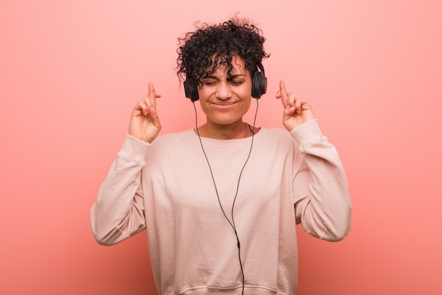 Joven mujer afroamericana escuchando música cruzando los dedos para tener suerte