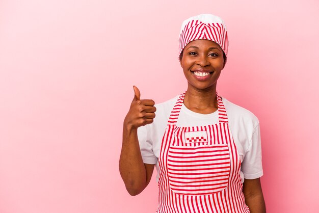 Joven mujer afroamericana fabricante de helado aislada sobre fondo rosa sonriendo y levantando el pulgar hacia arriba