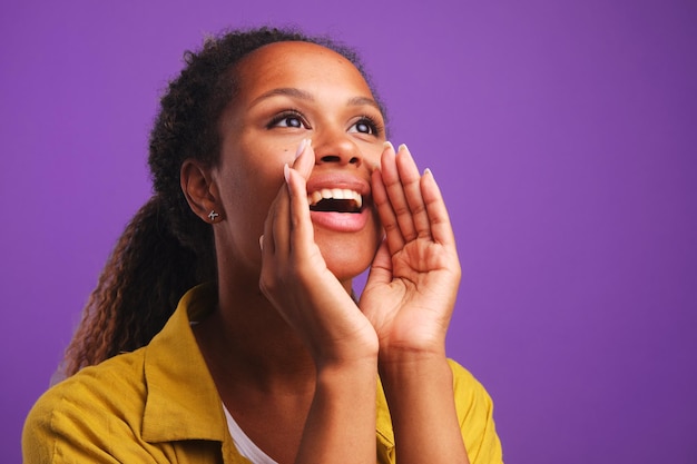 Joven mujer afroamericana gritando pide ayuda con las manos a la boca