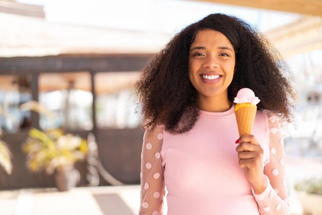 Joven mujer afroamericana con un helado de corneta al aire libre sonriendo mucho