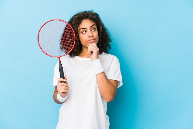 Joven mujer afroamericana jugando bádminton mirando hacia los lados con expresión dudosa y escéptica.