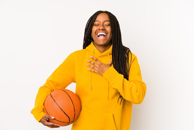 Joven mujer afroamericana jugando baloncesto aislado se ríe a carcajadas manteniendo la mano en el pecho.