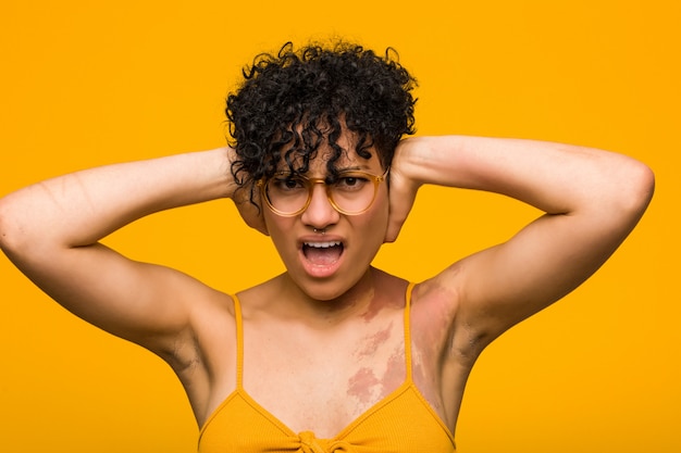 Joven mujer afroamericana con marca de nacimiento de piel cubriendo las orejas con las manos tratando de no escuchar un sonido demasiado fuerte.