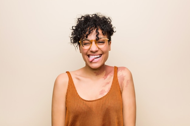 Foto joven mujer afroamericana con marca de nacimiento de piel divertida y amigable sacando la lengua.