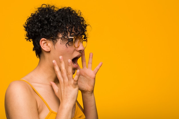 Joven mujer afroamericana con marca de nacimiento de piel grita fuerte, mantiene los ojos abiertos y las manos tensas.