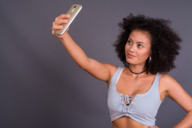 Joven mujer afroamericana multiétnica con cabello afro contra la pared gris