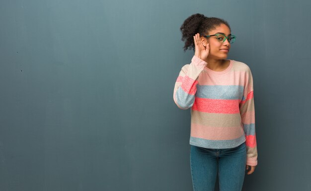 Joven mujer afroamericana con ojos azules intenta escuchar un chisme