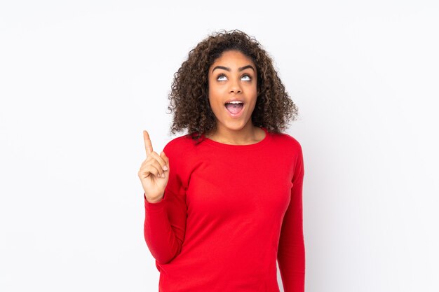 Joven mujer afroamericana en pared apuntando hacia arriba y sorprendido