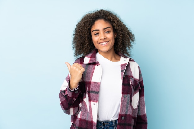 Joven mujer afroamericana en pared azul apuntando hacia el lado