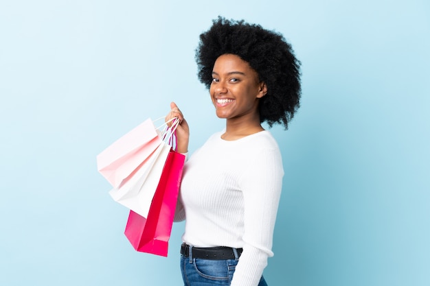 Joven mujer afroamericana en la pared azul con bolsas de compras y sonriendo