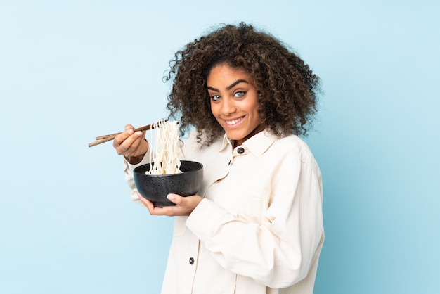 Joven mujer afroamericana en la pared azul con un tazón de fideos con palillos