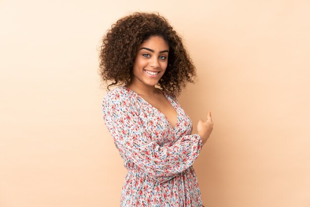 Joven mujer afroamericana en pared beige apuntando hacia atrás