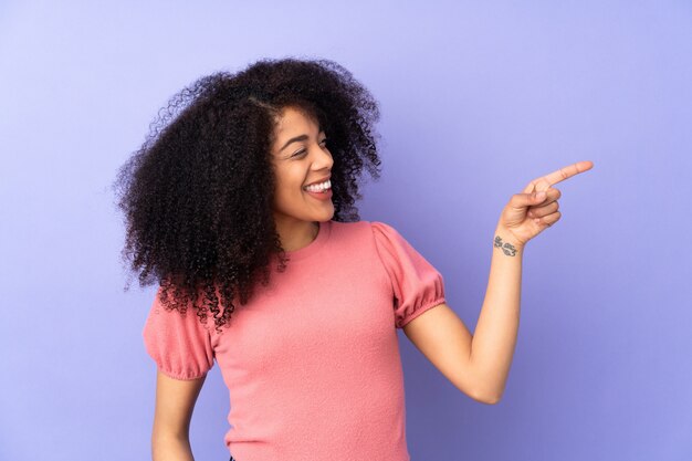 Joven mujer afroamericana en pared púrpura apuntando el dedo hacia el lado