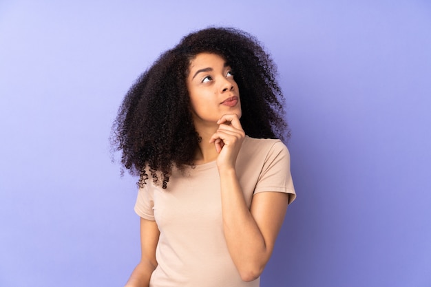 Joven mujer afroamericana en pared púrpura y mirando hacia arriba